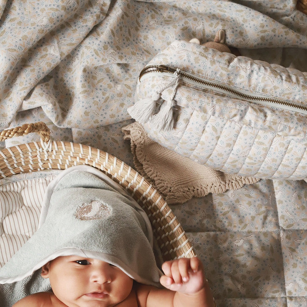 A baby wearing a hooded towel in quail design with wash bag nature trail beside