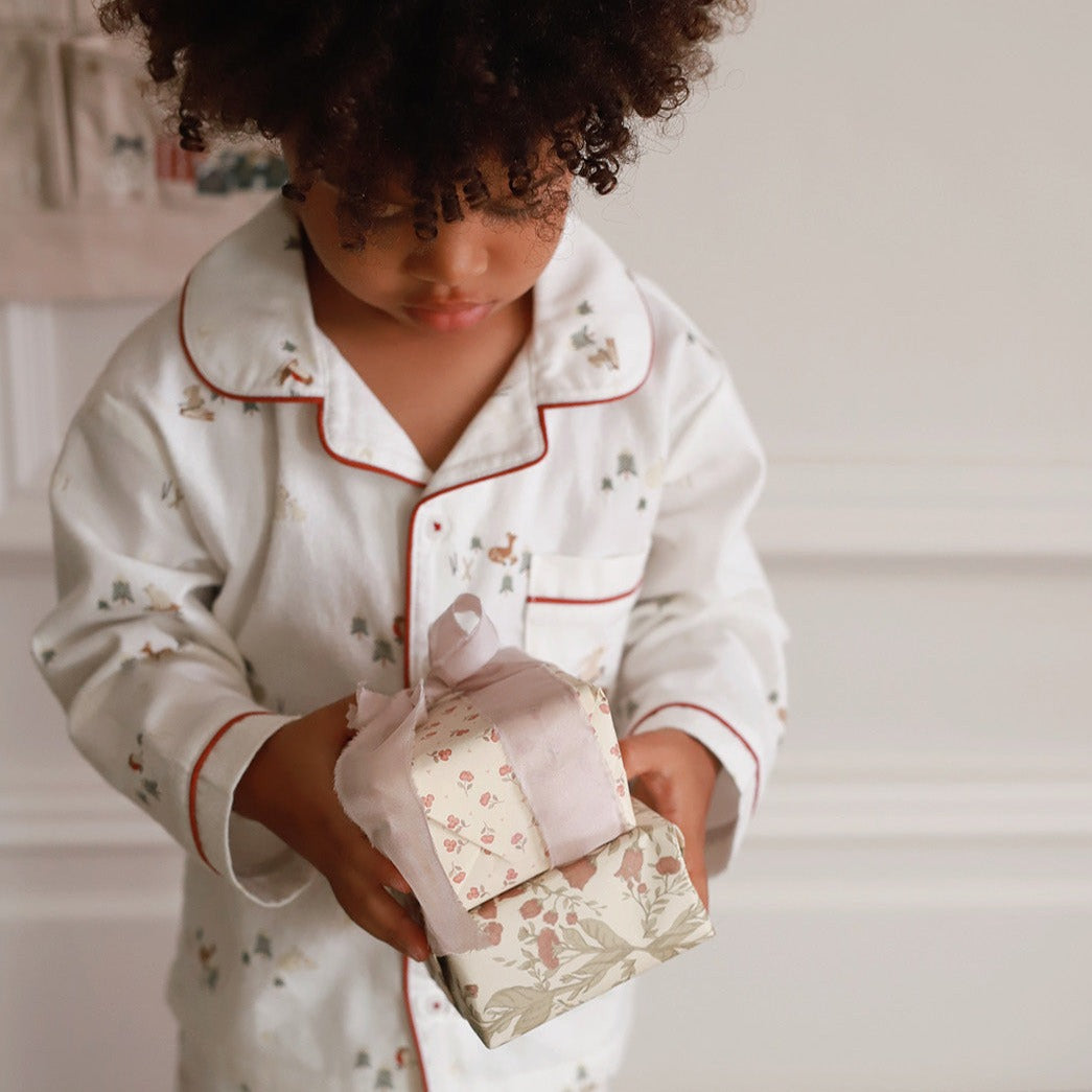 A boy wearing a nutcracker pyjamas holding a small chirstmas present