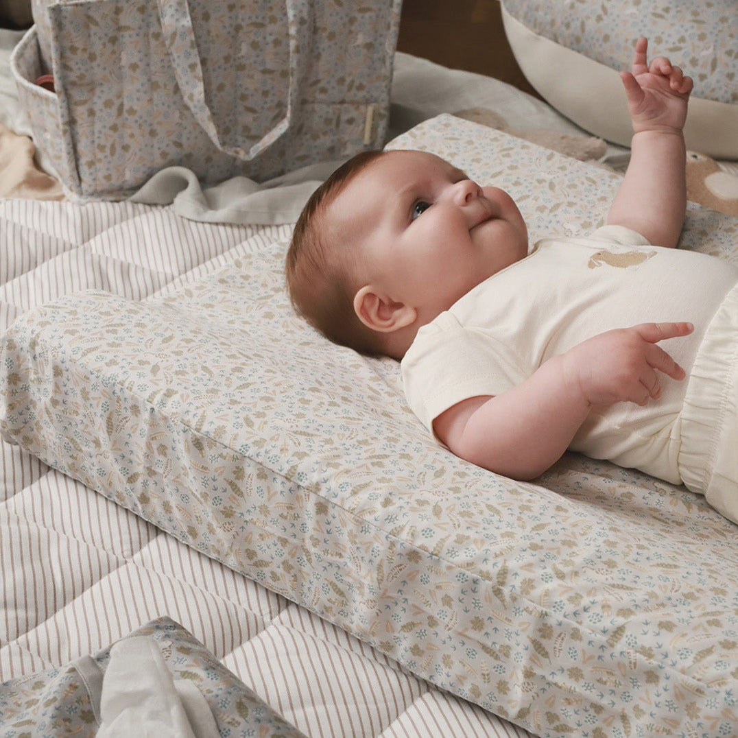Baby lying on a nature trail covered changing cushion